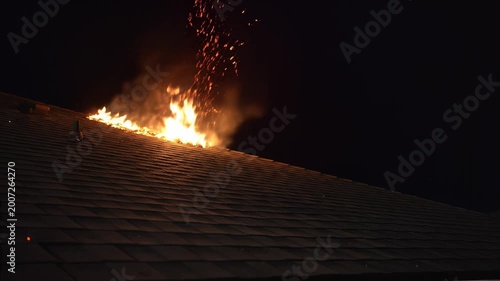 Dangerous roof fire ignites the nighttime sky with fiery sparks and intense heat