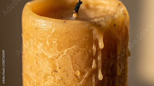 Close-up of a textured, amber-colored pillar candle with melted wax dripping down its side, showcasing the warm, cozy ambiance and the effects of burning