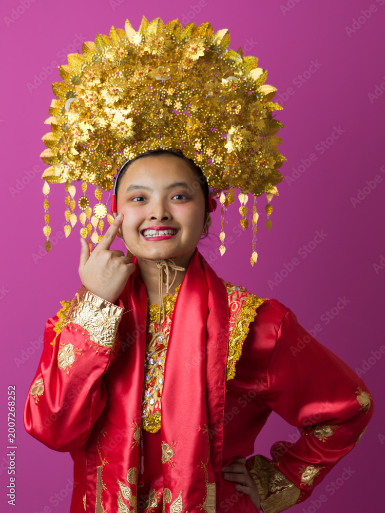 Fototapeta premium Young Indonesian Asian Woman Wearing Ornate Gold Headdress and Red Traditional Costume Celebrating Cultural Festival