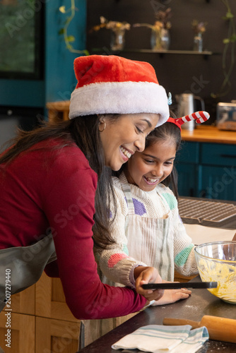 Indian mother and daughter mixing batter at home kitchen counter with Santa hat, aprons, spatula