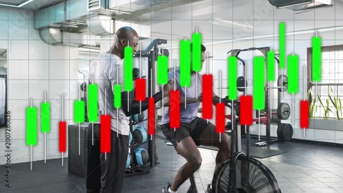 Trainer walking up to trainee riding fan bike, coaching form for fitness while overlay tracking rpm