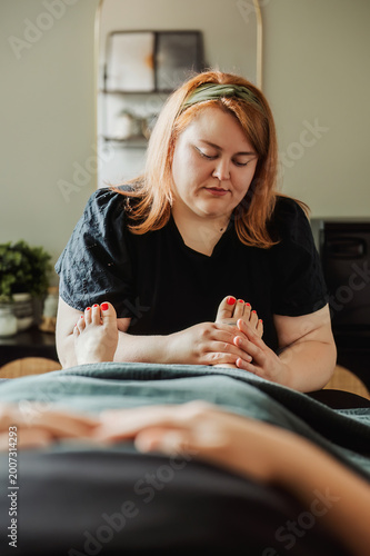 Therapist holding client's feet on massage table, styled interior