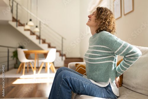 Fotografie Woman suffering from back pain sitting on sofa