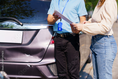 Insurance agent and woman inspecting car damage after accident