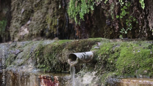 Raw 4K footage of mountain water flowing from a pipe at a natural spring in Uttarakhand, showing clean fresh source, mossy rocks, and peaceful rural environment.