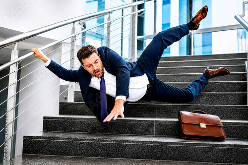 Businessman falling on office stairs during workplace accident with briefcase