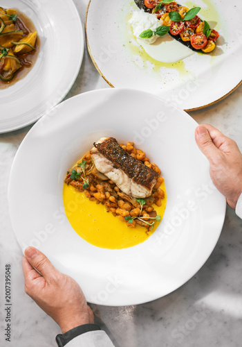 Hands serving gourmet fish dish with sauce and gnocchi in fine dining setting