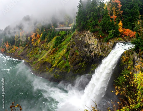Lush, mist-shrouded waterfall cascades down a rocky cliff adorned with autumn foliage