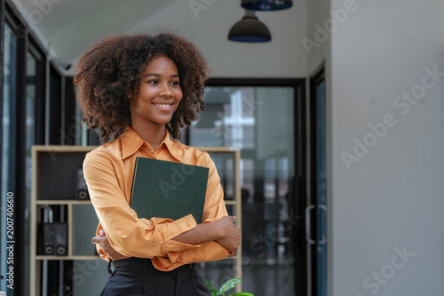 Smiling African American young woman holding notebook and looking away in modern office.