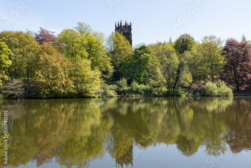 Church and trees reflected in the water of Lymm Dam in Cheshire on a sunny spring day
