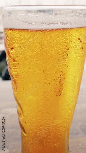 Cold pint of refreshing golden lager beer showing condensation droplets on glass during summer season.