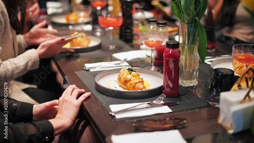 People photographing gourmet croissant dish with phones at elegant diznner table setting.