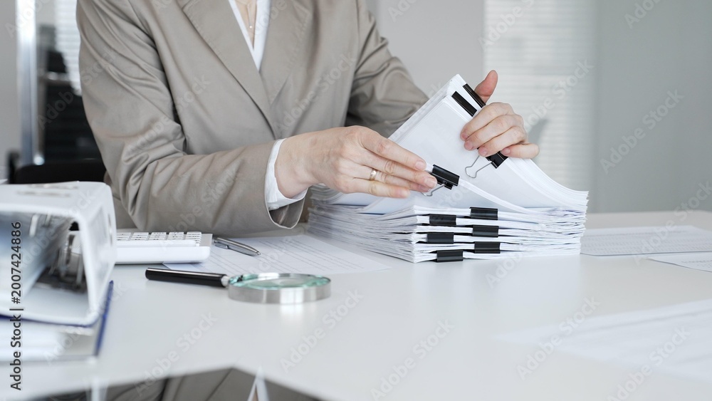Fototapeta premium Businesswoman hands organizing financial documents stack on office desk, managing paperwork, bookkeeping, and administration. Audit and taxes concept