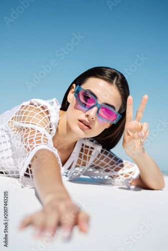 Stylish Young Woman in Sunglasses Showing Peace Sign Against Blue Sky