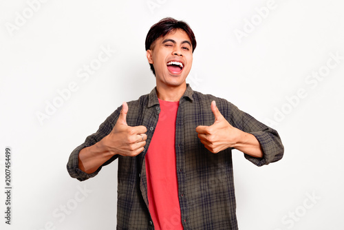Fotografie Smiling winking young Asian man giving two thumbs up and laughing in approval fo