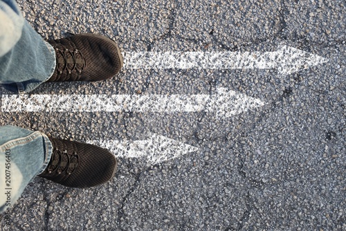 Feet standing on road with multiple arrows directions confusion choice concept top view