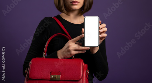 Woman holding smartphone with blank screen and red handbag against purple background