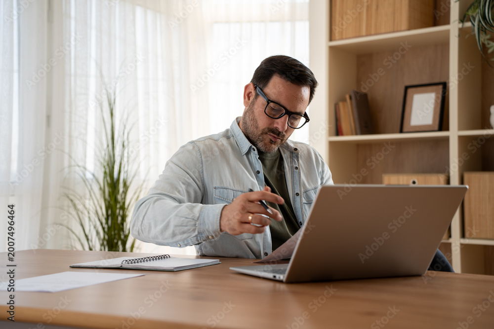 Fototapeta premium Focused male professional working remotely on laptop at home desk