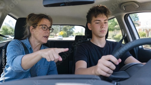 Teenager Boy Taking a Driving Lesson with Mature Woman Instructor or Mother in a Car