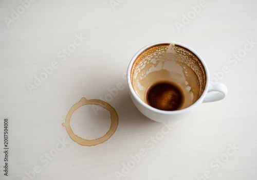 Top View of an Empty White Coffee Cup with Brown Residue and a Coffee Ring Stain on a White Table Surface