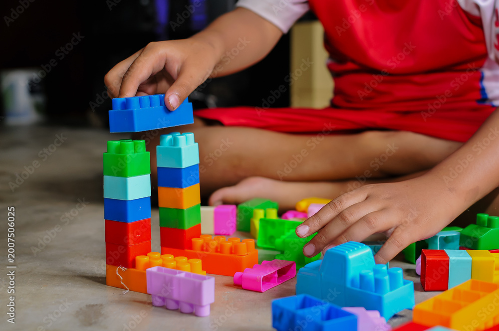 Naklejka premium Close-up of a child’s hands playing with colorful building blocks (LEGO-style toys). The image highlights creativity, learning through play, and fine motor skill development in early childhood