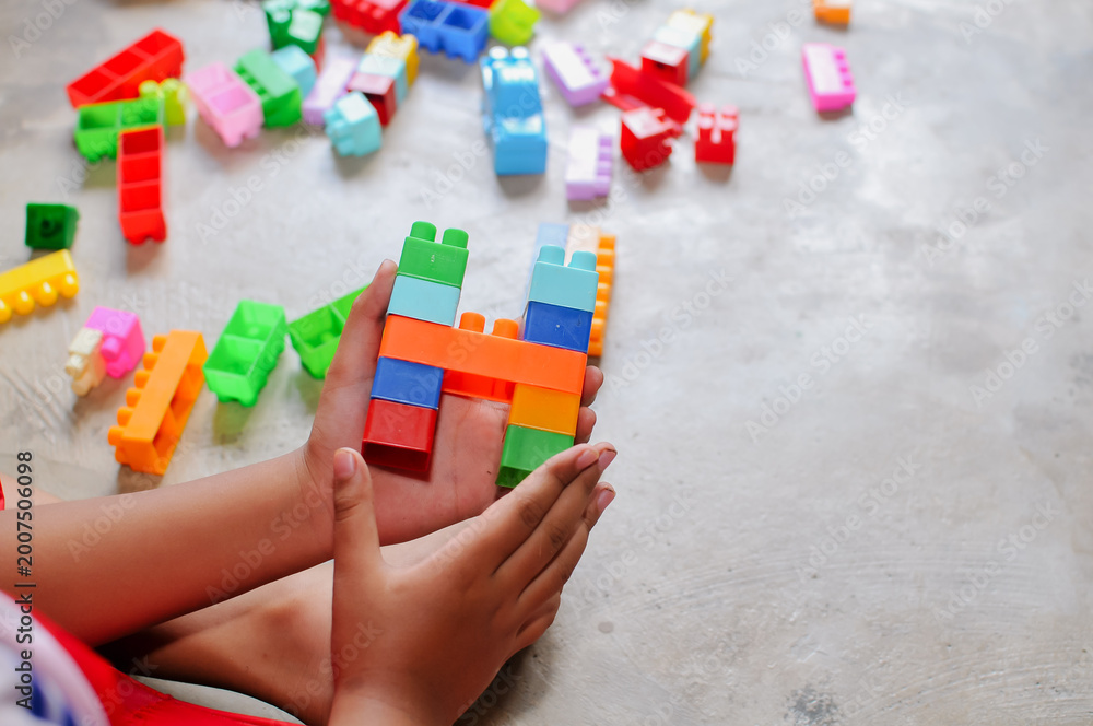 Naklejka premium Close-up of a child’s hands playing with colorful building blocks (LEGO-style toys). The image highlights creativity, learning through play, and fine motor skill development in early childhood. Bright