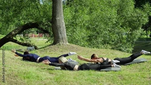 Three friends doing fitness workout in park on summer day. Young athletic women doing core exercise outdoors lying on yoga mat in summer park. Healthcare concept. 4K, UHD