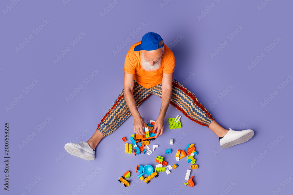 Obraz premium Older man with orange shirt and striped pants enjoys building with colorful blocks on a purple backdrop, a playful, carefree vibe that feels creative and hipster-inspired