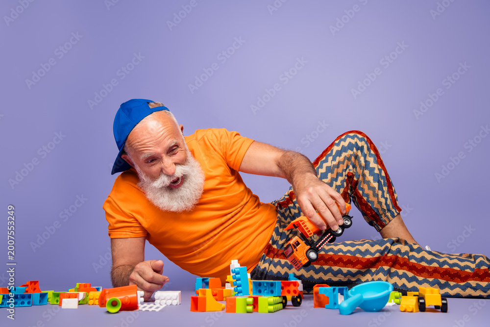 Obraz premium Elderly man in orange shirt with striped pants plays with colorful blocks on a purple background, capturing a playful, carefree moment