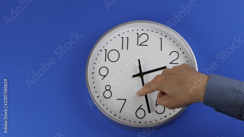 Change the time clocks hour 3 to hour 2. Man's hand moves the hand to change the time, on blue background