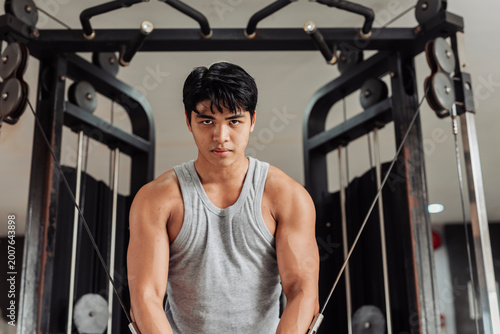 Young Asian man does cable crossover at the gym, holding peak contraction to highlight chest muscle definition and controlled resistance technique.