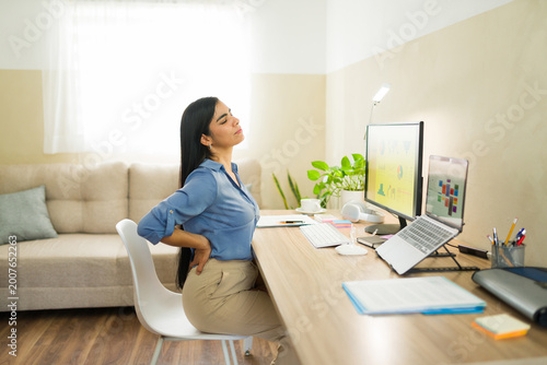 Businesswoman experiencing back pain while working at home, suffering from bad posture and ergonomics