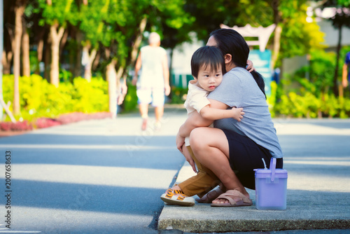 A heartwarming moment of an Asian mother hugging her young son in a public park, showing love, protection, and family bonding during an outdoor walk.
