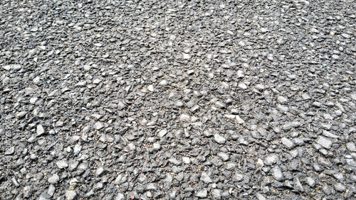 Photos High-angle close-up of rough dark gray asphalt road surface texture, grainy bitumen pavement background with crushed stones and gravel details