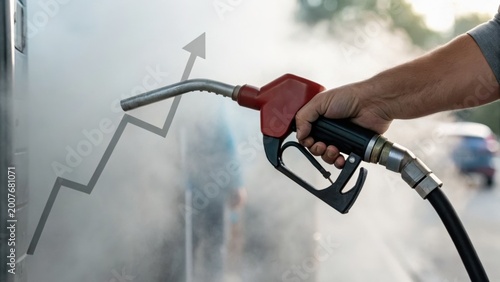 A hand holds a fuel pump nozzle at a gas station, with a rising arrow symbolizing increasing fuel prices or demand.