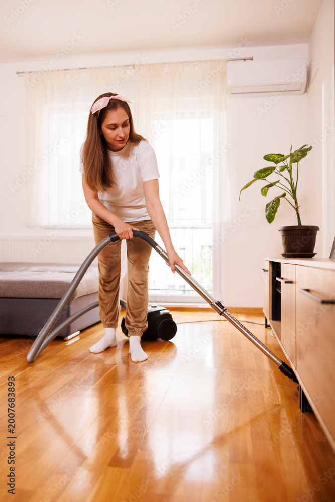 Fototapeta premium Woman vacuum cleaning floors while deep cleaning the house