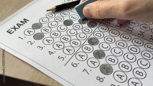 Hand erasing wrong answer on multiple choice exam sheet. Concept of correction, testing, education, mistake, and academic evaluation
