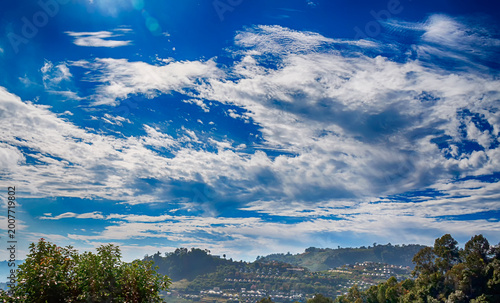 Vibrant blue sky filled with white clouds above a verdant mountain and small village resort.