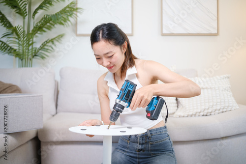 Fotografie Young woman assembling furniture at home using a cordless drill, focused on DIY