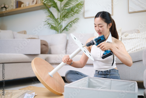 Young woman assembling furniture on the floor using a cordless drill. DIY lifestyle concept.