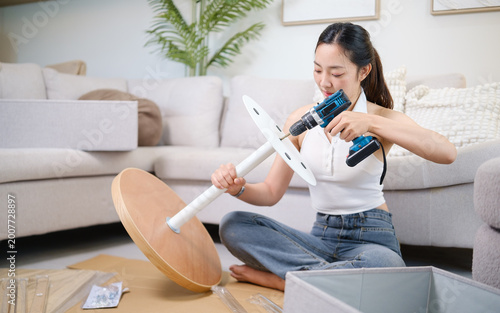 Young woman assembling furniture on the floor using a cordless drill. DIY lifestyle concept.