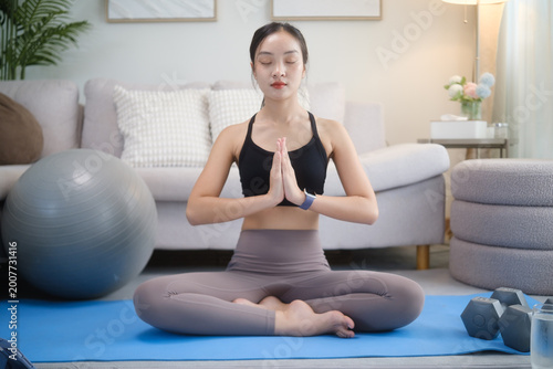 Young woman meditating at home, practicing mindfulness and relaxation on a yoga mat in a living room. Healthy lifestyle concept. Free Download Young woman meditating at home, practicing mindfulness and relaxation on a yoga mat in a living room. Healthy lifestyle concept. - GFXLoad