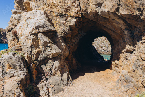 Fotografie Natural tunnel through a rugged rock formation leading to the turquoise sea at C