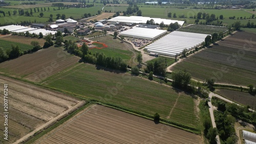 Fotografía Agricultural Aerial View: An expansive view of a modern agricultural complex nestled amidst fertile fields, with greenhouses, open farmlands, and infrastructure