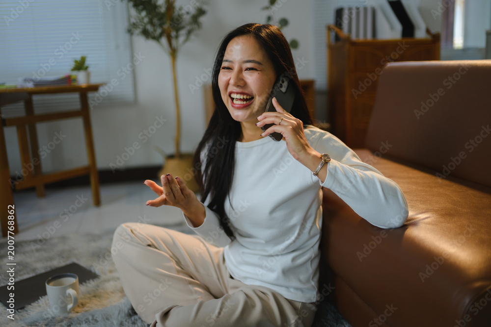 Obraz premium Young Asian woman laughing talking on mobile phone at home