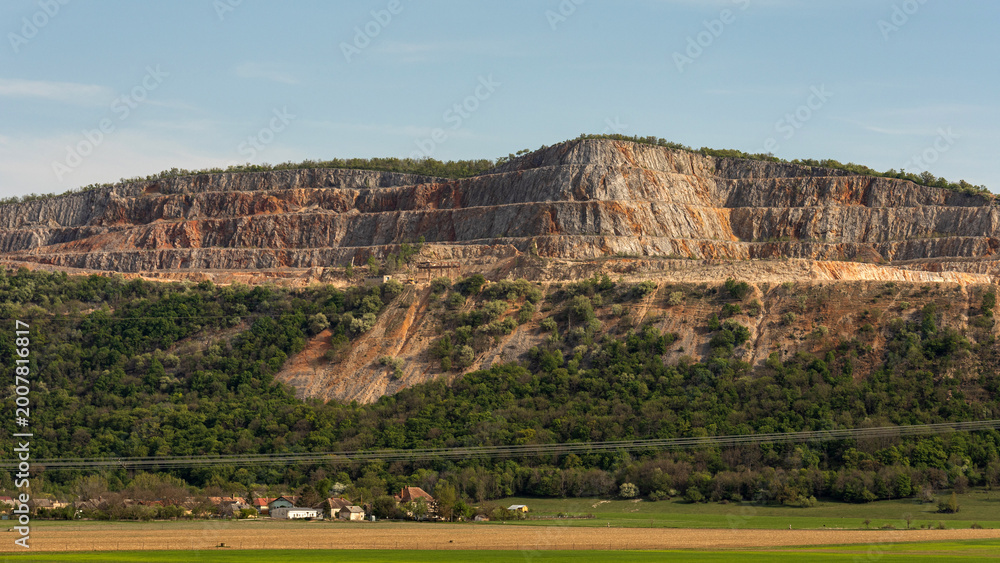 Fototapeta premium Large rock formation with steep cliffs and plants in the background near a small town in daylight