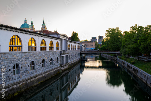 Foto Riverside architecture and reflections along the Ljubljanica River in Ljubljana during sunset, featuring historic buildings, calm water and urban travel atmosphere in Slovenia