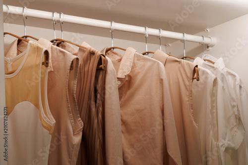 female clothes in beige, white and pastel earth tones hanging on rack in closet at home or fashion shop. Minimalist capsule wardrobe organization and modern women fashion collection concept.
