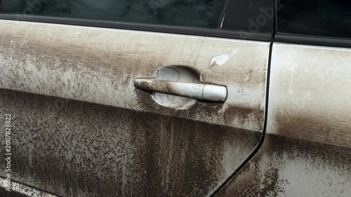 Close-up of a muddy car door covered in dirt and road grime after driving in harsh weather conditions. Detailed texture of splashes and stains highlights vehicle maintenance and car wash concept.