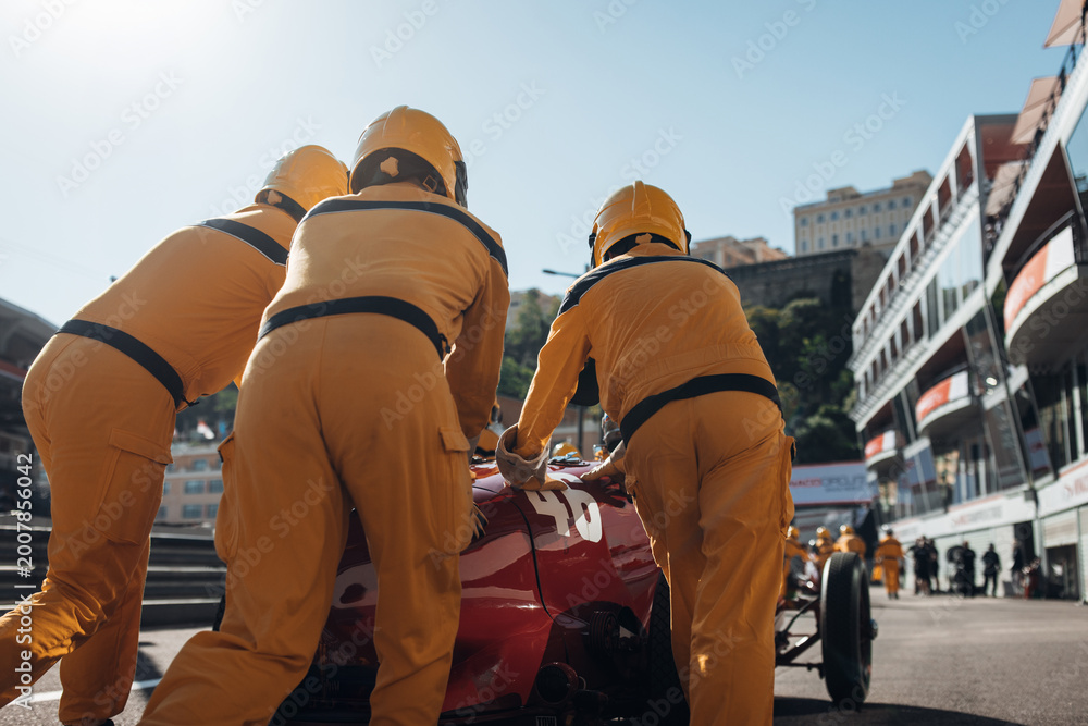 Fototapeta premium Team mechanics pushing a historic Formula 1 car along the pit lane during a classic racing event